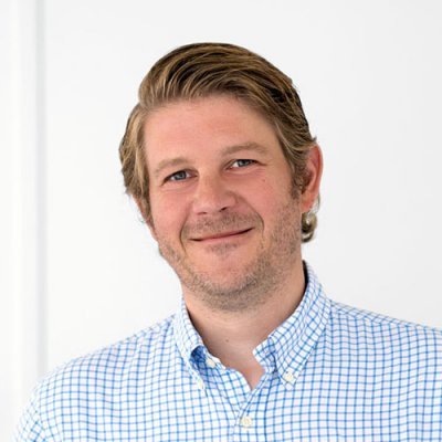Portrait of a smiling man, Florian Lage, in a white shirt with checkered blue lines.